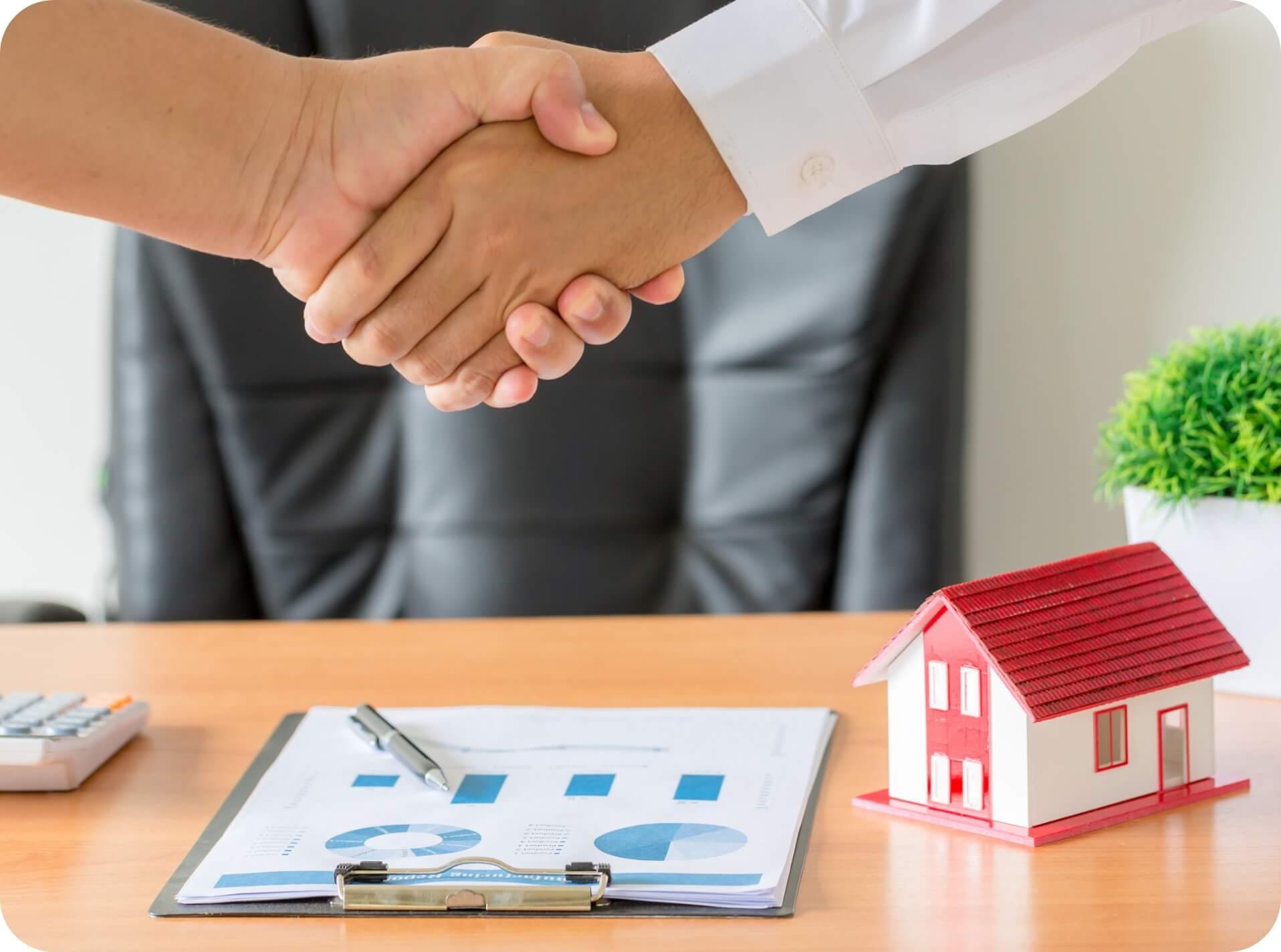 Two people shaking hands while signing contract